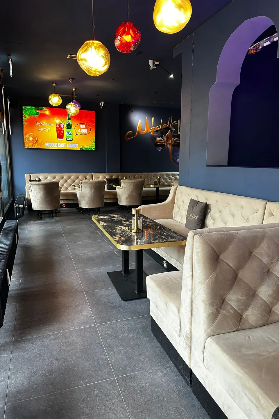 Klassische Lounge mit hellen Polstersofas, Marmortischen und bunten Hängelampen